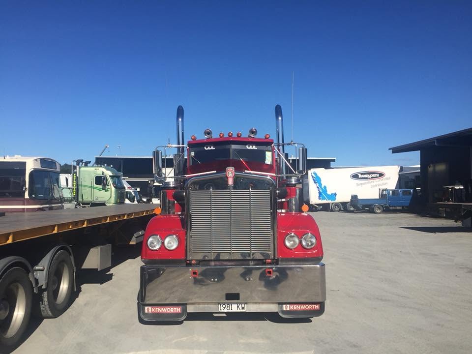 Classic red Kenworth truck parked in the yard alongside a flat deck trailer